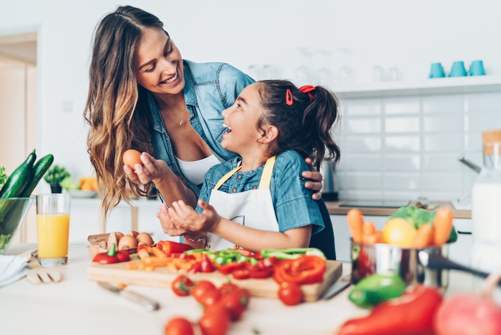 Woman and girl child in kitchen preparing vegetables to cook.