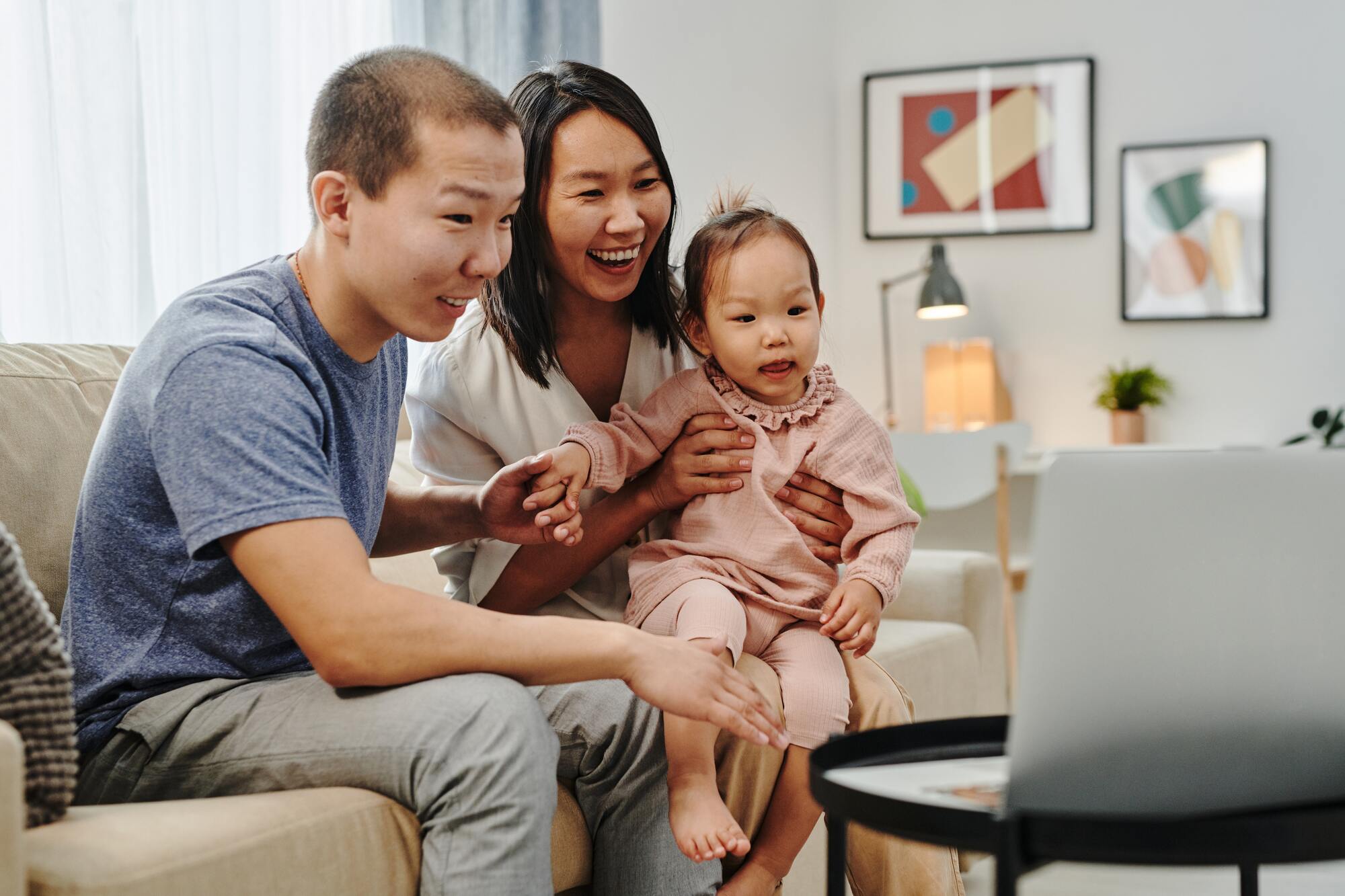 Happy Asian parents holding baby to computer screen in a video call.