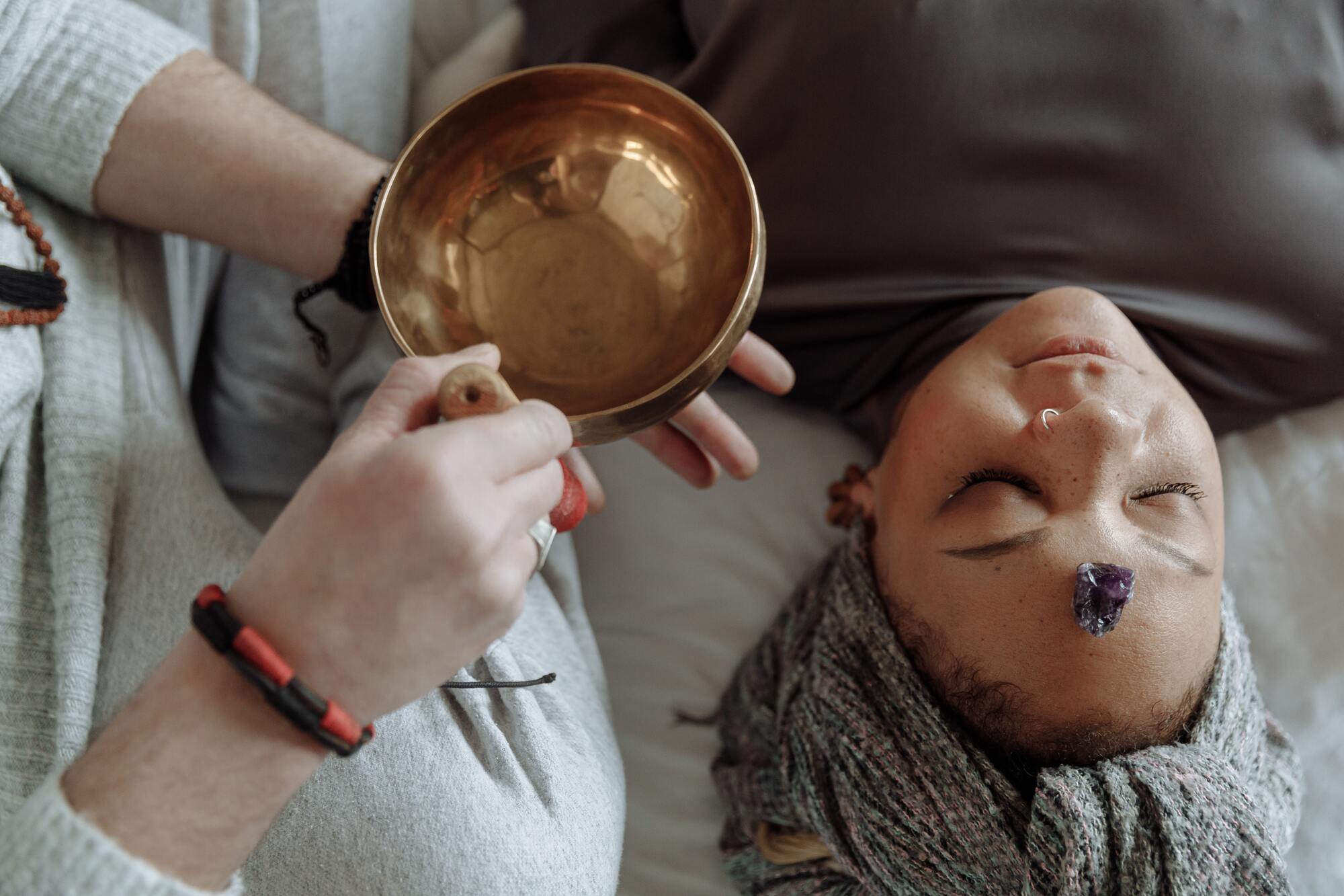 Woman laying on floor with eyes closed peacefully, with an amethyst crystal on her forehead, in a sound healing session.