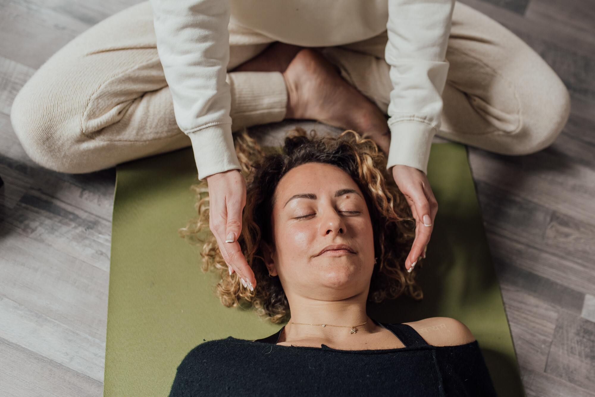 Woman laying on floor with eyes closed peacefully, in a reiki therapy session.