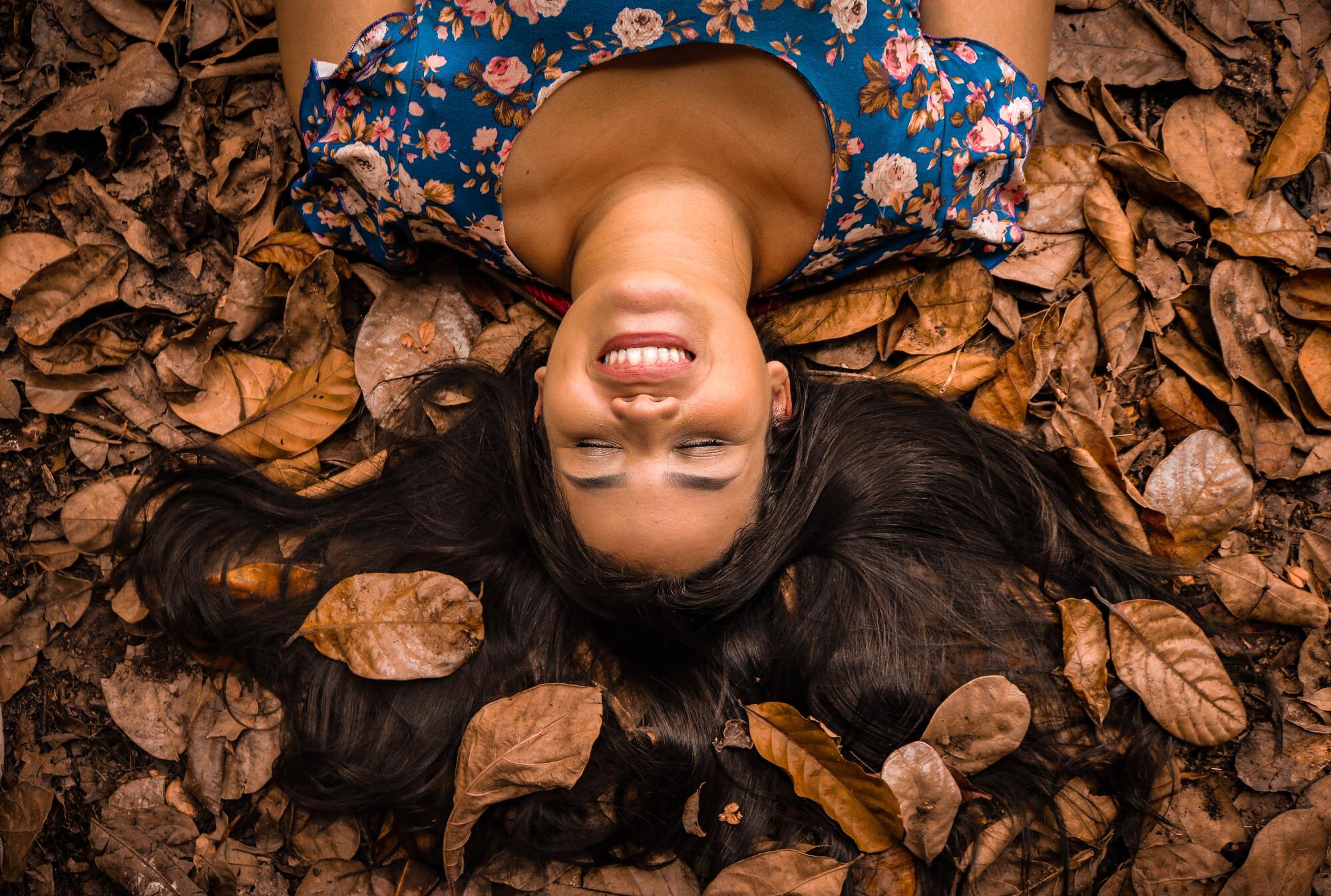 Woman laying in a pile of autumn leaves smiling.