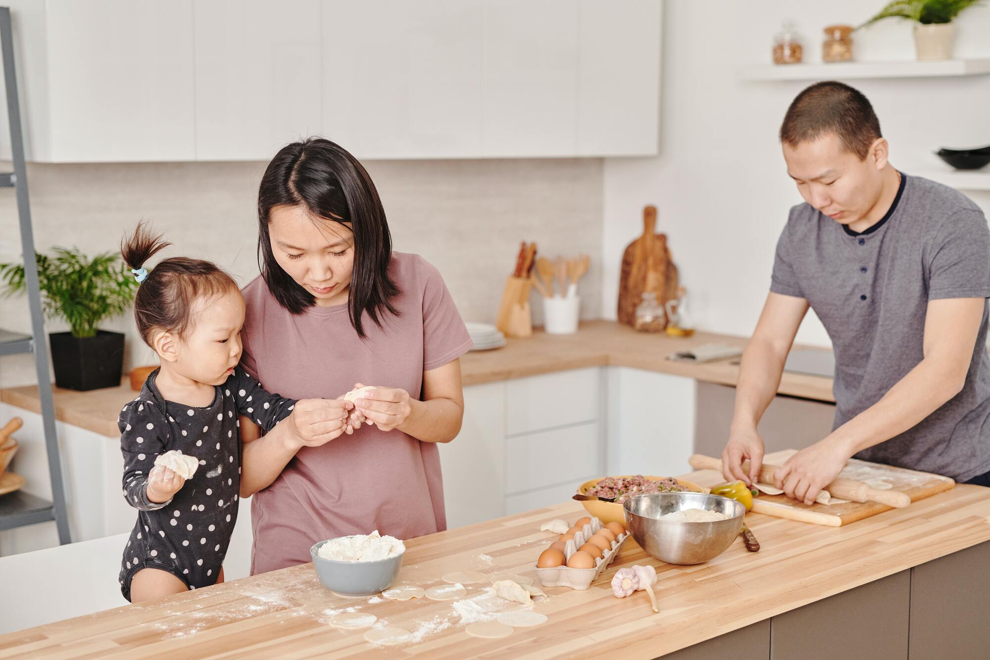 Asian parents cooking in their kitchen with their baby. This image is used to display maintaining cultural identity in your diet.