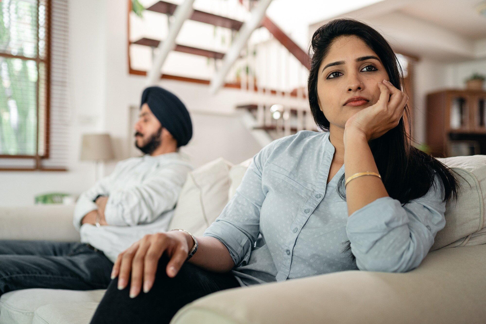 Woman in a relationship sitting on a couch with frustrated partner.