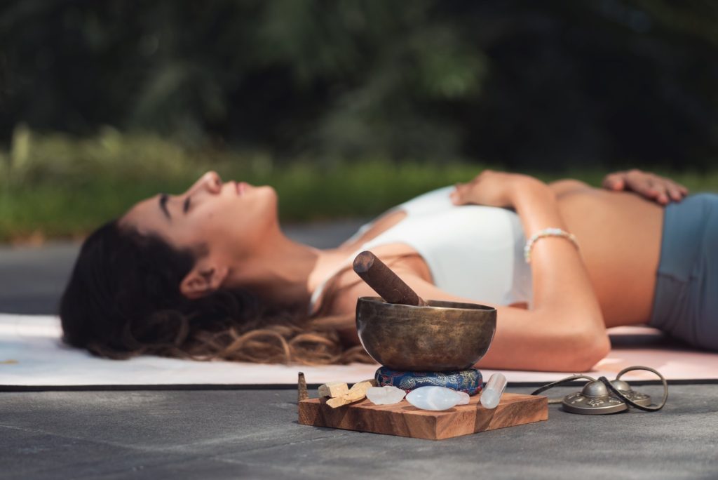 Woman laying next to a sound bowl and chakra crystals, engaging in a sound healing session.